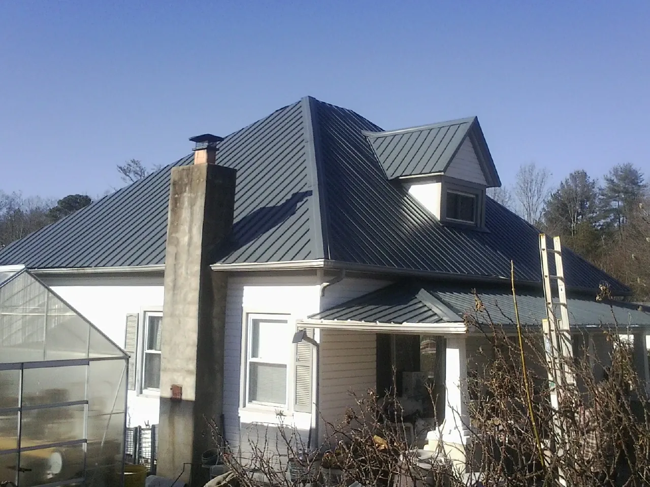 Dark blue standing seam metal roof on a white farmhouse with dormer — Slate & Tile Roof Repair by Roofing Brothers in Kettle Falls