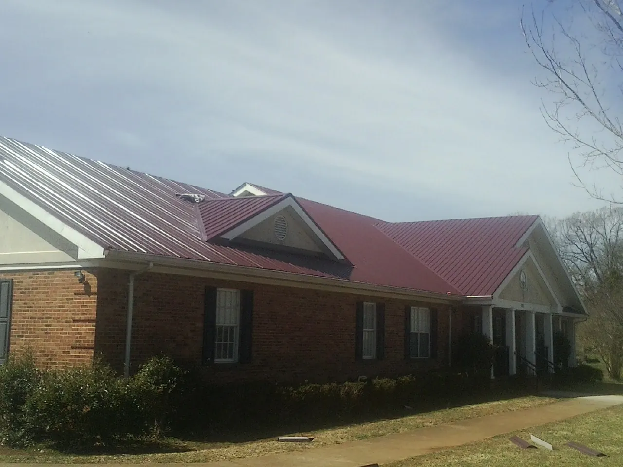 Red metal roof with gabled entries on a long brick building, from a Hail Damage Roof Repair job in Kettle Falls