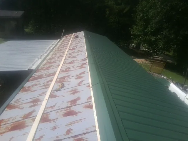 Old rusted panels beside newly installed green metal roofing — Wind Damage Roof Repair by Roofing Brothers in Kettle Falls