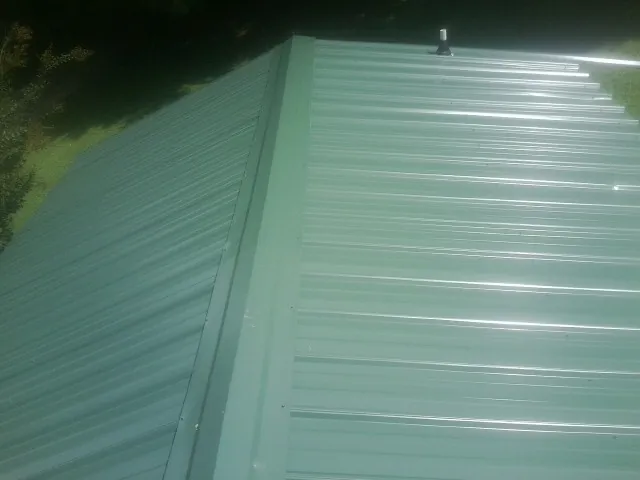 New green metal panels meeting at the ridge of a roof — Flat Roof Repair work by our crew in Kettle Falls
