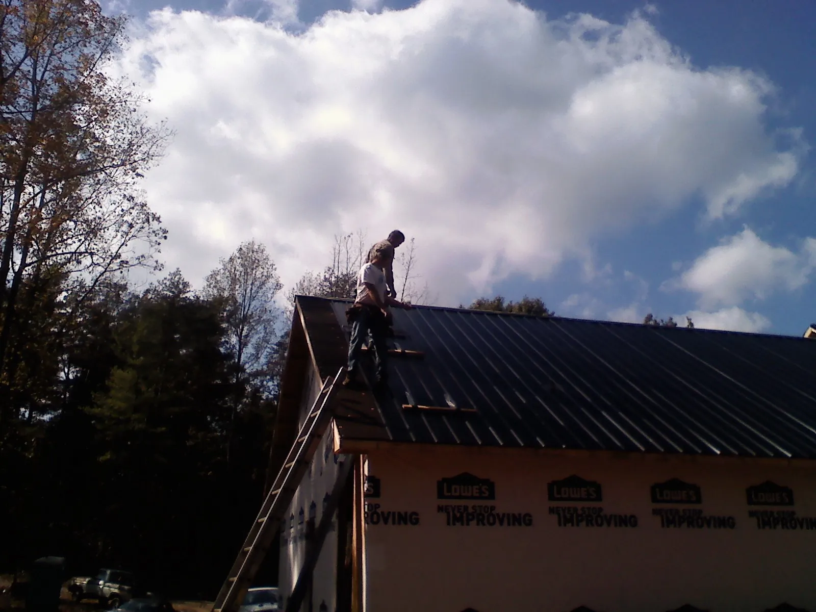 Roofer fastening dark metal panels high against a cloudy sky, from a Roof Inspection job in Kettle Falls