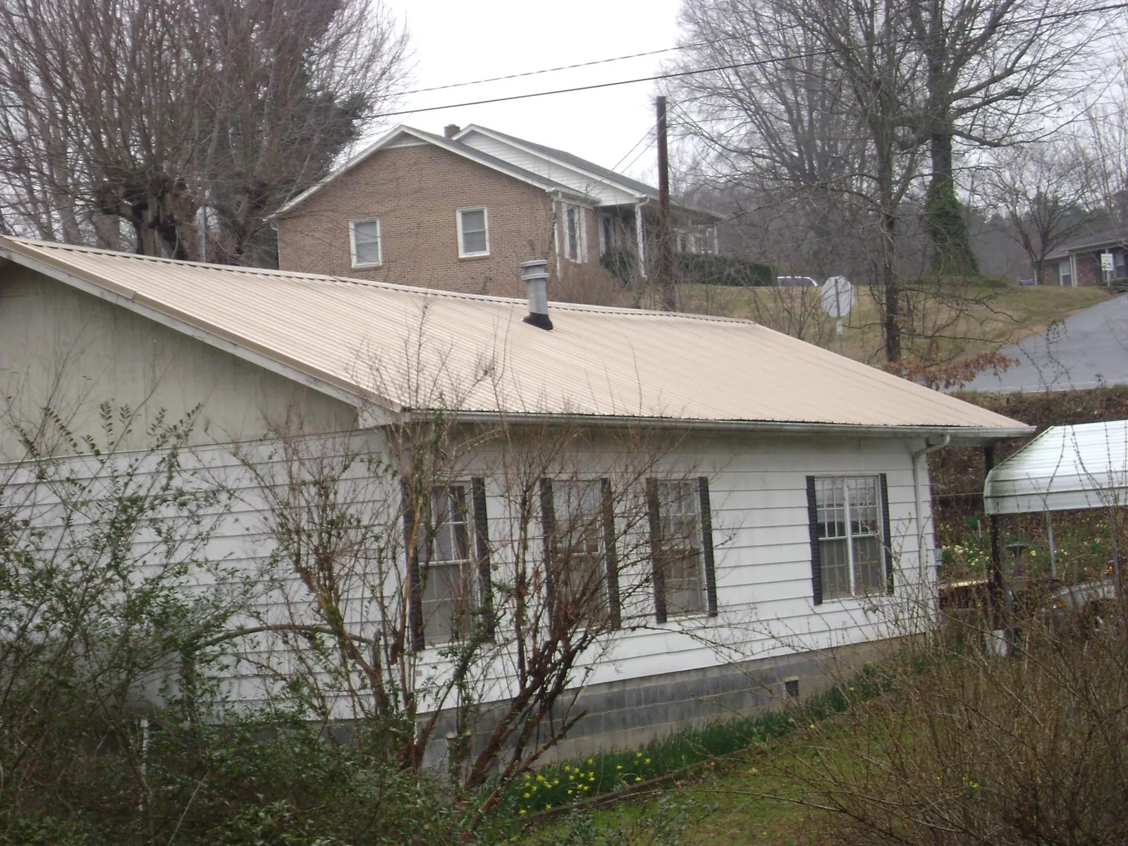 Tan metal roof on a white sided house set into a hillside — Commercial Roofing by Roofing Brothers in Kettle Falls