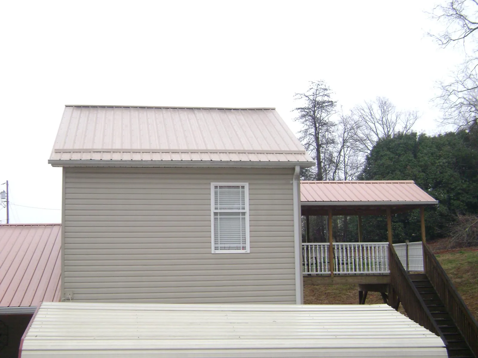 Tan metal roofs on a two story addition and attached porch, from a Roof Replacement job in Kettle Falls